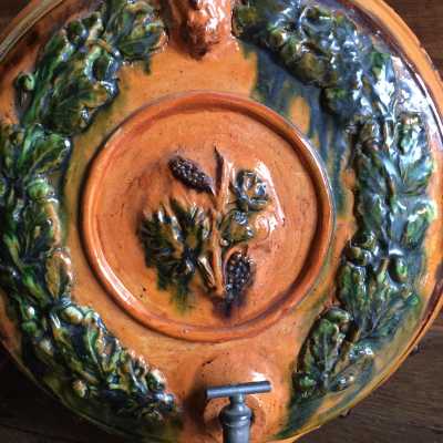 Applied decoration, crown of oak leaves with acorns around a central medallion decorated with a vine branch with grapes surmounted by a half-humped face of fauna, all surrounded by small spherical cabochons at the circular edge