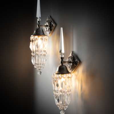 Mark Brazier-Jones' "Libertine" wall sconces illuminated on a dark wall, three-quarter view.